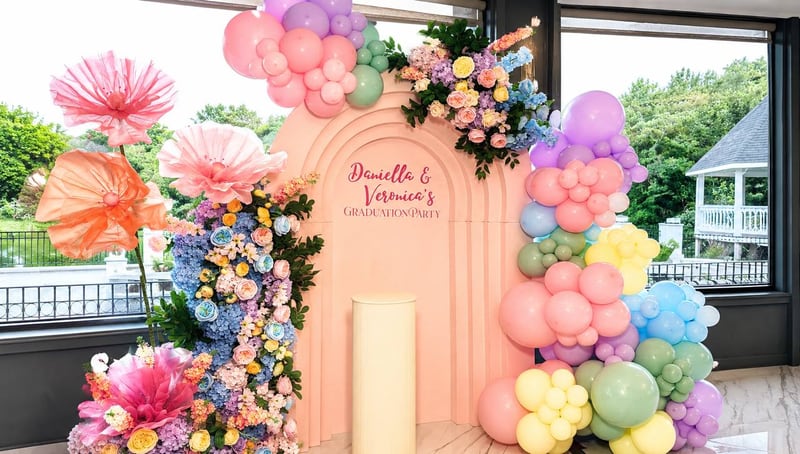 Pastel balloon garlands, oversized paper flowers and a peach arch backdrop beside large windows