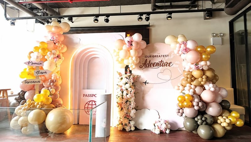 Adventure-themed backdrop with a cream arch, a passport prop, destination signs and neutral, blush and gold balloon garlands